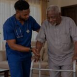 Young Nigerian male nurse helping an elderly man walk safely at home with a walker.